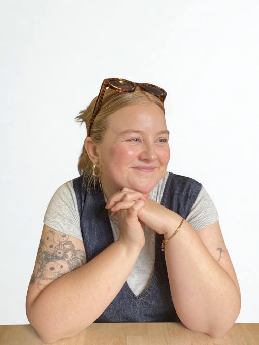 A profile photo of a woman looking off to the side in a white and blue top with tied back blonde hair and sunglasses on her head. 