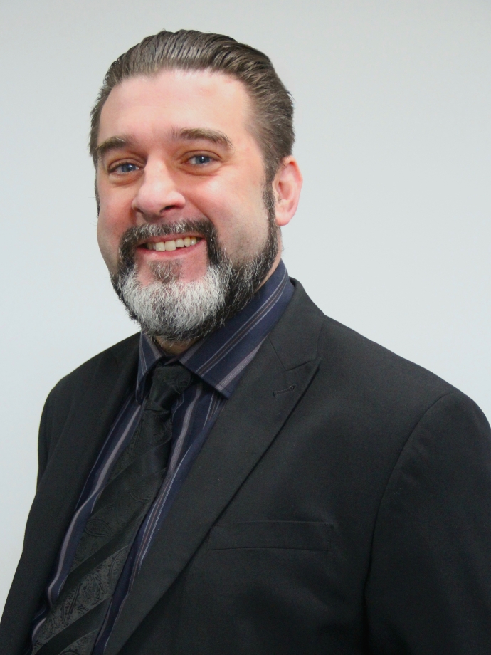 A photo of a man with a beard who is wearing a black shirt and jacket.