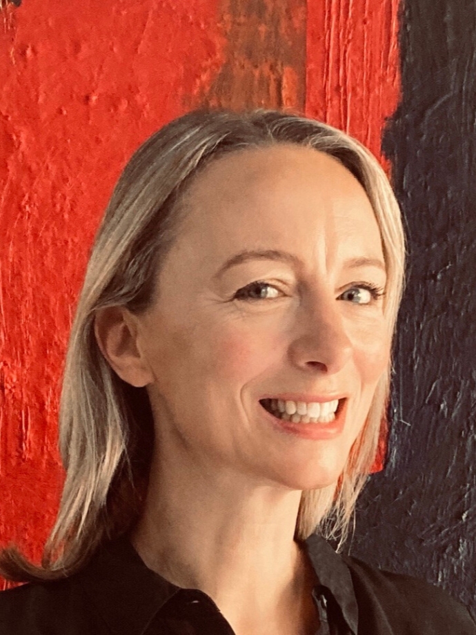 Woman with shoulder-length hair in a dark shirt standing in front of a red and black wall.