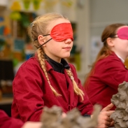 Students in red smocks shaping clay sculptures in an art classroom.